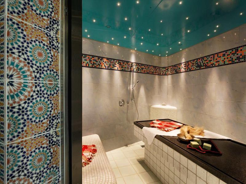 Innenraum eines Hammams mit verzierten Fliesen, zwei Liegen und sanfter Beleuchtung an der Decke.