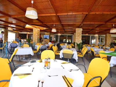 Offenes Restaurant mit gelben Stühlen und gedeckten Tischen unter Holzdach.