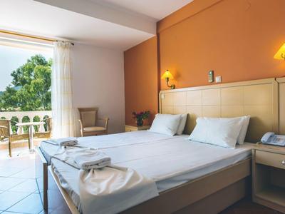 Helles Hotelzimmer mit Doppelbett, orangener Wand und Balkon mit Aussicht auf Grün.