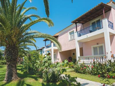 Ein pinkfarbenes Hotelgebäude mit Balkonen, umgeben von Palmen und üppigem Grün bei blauem Himmel.