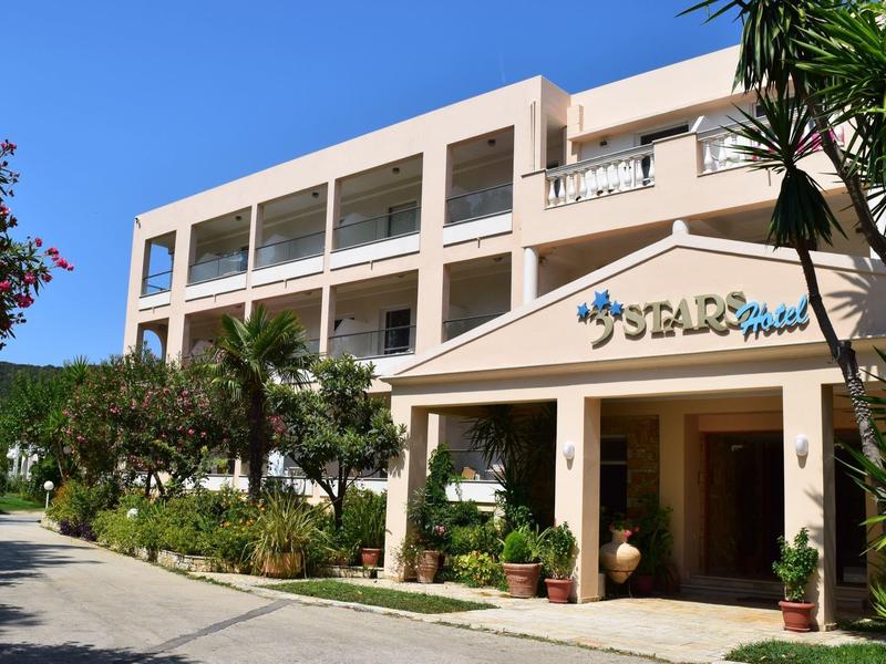 Hoteleingang mit Palmen und breitem Weg, mehrstöckiges Gebäude im Hintergrund.