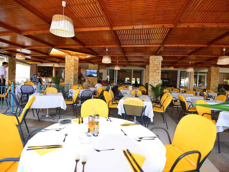 Offenes Restaurant mit gelben Stühlen und gedeckten Tischen unter Holzdach.