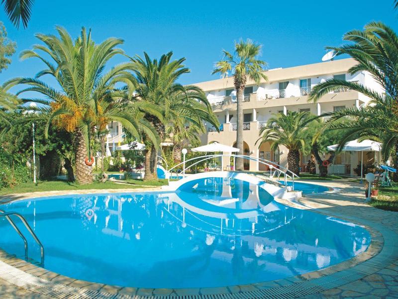 Runder Hotelpool umgeben von Palmen und Liegestühlen unter klarem blauem Himmel.