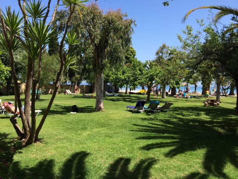 Grüner Hotelgarten mit Liegestühlen, Bäumen und Meer im Hintergrund.