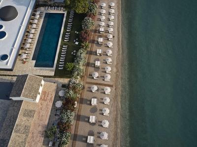 Vogelperspektive auf Strand mit Liegestühlen, Pool, Gebäude und angrenzendem Meer.