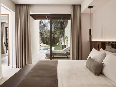 Modernes Schlafzimmer mit großem Fenster, Vorhängen, weißer Bettwäsche und Zugang zu Terrasse mit Liegestühlen.