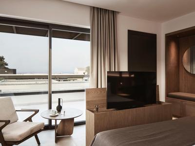 Modernes Schlafzimmer mit Balkon, hellen Wänden, braunen Möbeln und großem Fernseher.