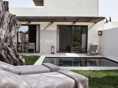 Moderner Garten mit Pool, Liegestühlen und großer Baumwurzel neben weißem Haus und Glas-Schiebetür.