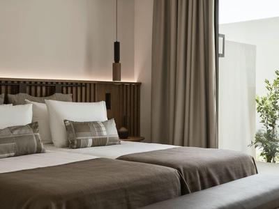 Modern eingerichtetes Hotelzimmer mit Doppelbett, braunen Vorhängen und Balkon mit Pflanzen.