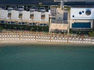 Luftaufnahme eines Hotels am Strand mit Reihen von Sonnenschirmen und Liegen entlang des Wassers.