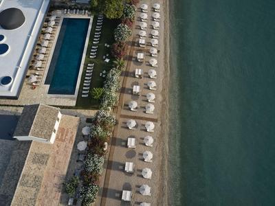 Blick von oben auf Hotelpool, Liegestühle und Strand neben ruhigem Wasser.