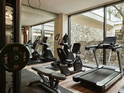Modernes Fitnessstudio mit Laufband, Ergometer und Gewichten, durch großes Fenster heller Raum.