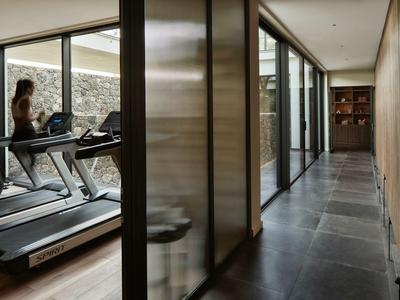 Moderner Fitnessraum neben einem langen Flur mit dunklem Bodenbelag in einem Hotel.