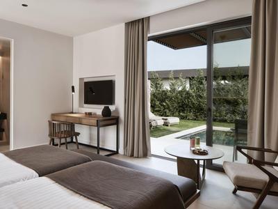 Modernes Hotelzimmer mit zwei Betten, Schreibtisch und Blick auf Terrasse und Garten.