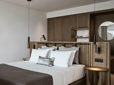 Modernes Hotelzimmer mit großem Bett, Holzelementen und rundem Spiegel an der Wand.