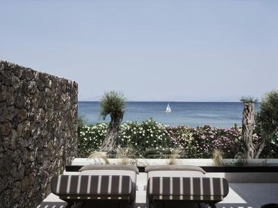 Zwei Liegestühle mit Kissen auf einer Terrasse mit Meerblick und Segelboot am Horizont.