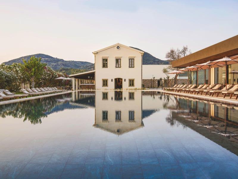 Velký bazén s lehátky kolem a bílá budova v pozadí, pod jasnou oblohou.