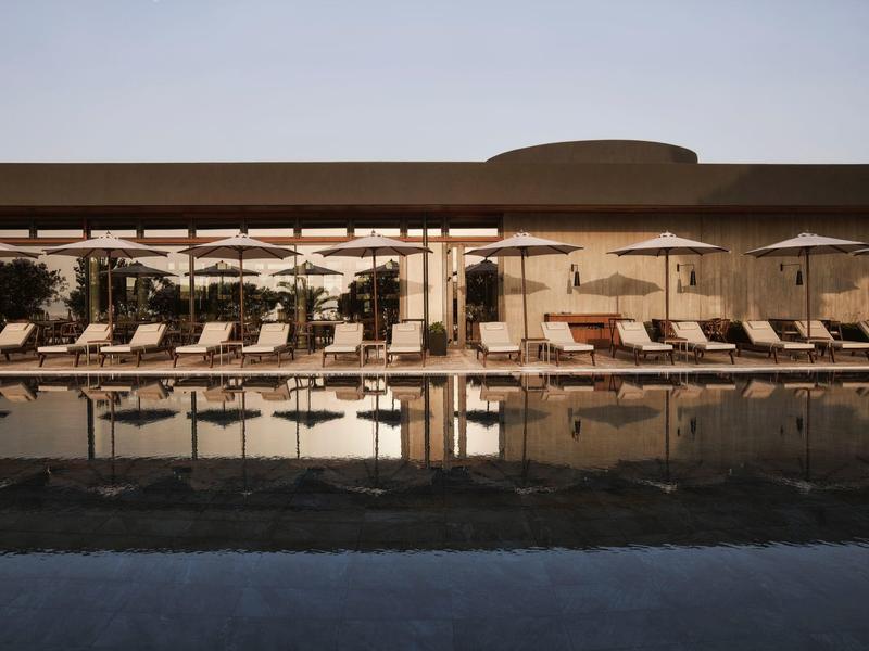 Hotelový bazén s lehátky pod pergolou při západu slunce.