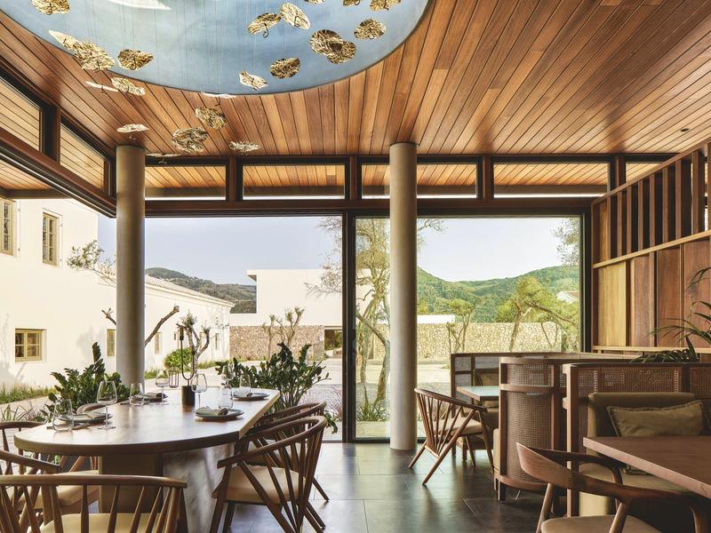 Interiér restaurace s dřevem, velkými okny a stropem zdobeným malovanými ptáky.