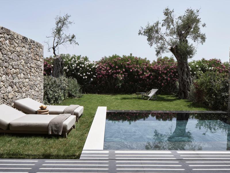 Klidný bazén obklopený kamennými zdmi, dvě lehátka a kvetoucí zahrada.