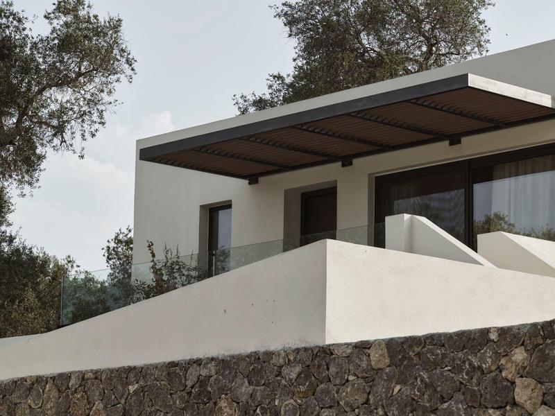 Moderní terasa s kamenou zdí a pergolou ve vile obklopené stromy.