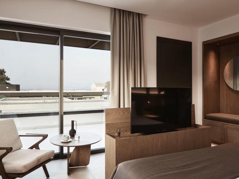 Moderní hotelový pokoj s balkonem a výhledem na moře, zařízený v neutrálních tónech.