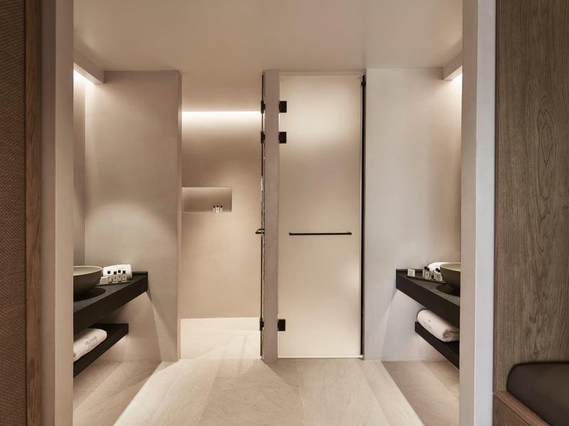 Moderní hotelová chodba s béžovými stěnami, černými policemi a decentním osvětlením.