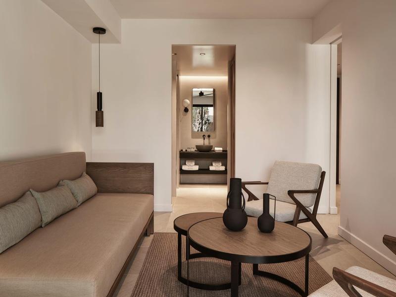 Obývací pokoj v moderním hotelovém pokoji s béžovou pohovkou a kulatým stolkem.