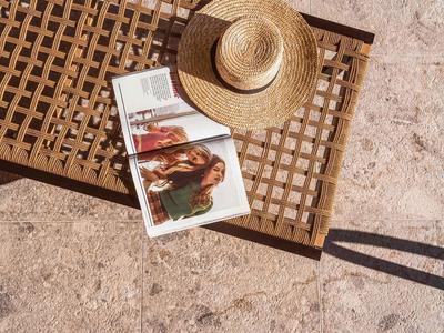 Lettino in legno con cappello di paglia e rivista aperta su terreno sabbioso