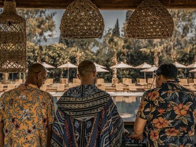 Tre uomini con camicie colorate seduti a un bar con vista sulla piscina e lettini.