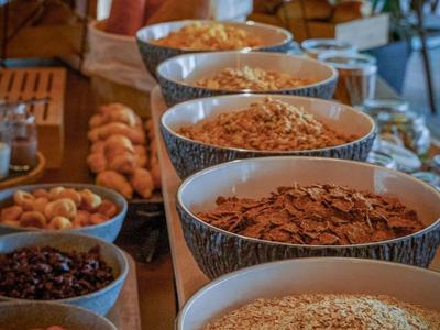 Ciotole con vari cereali per colazione e frutta secca su un tavolo di legno in una stanza luminosa.