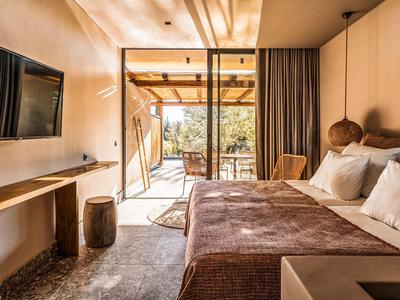 Camera d'hotel accogliente con letto matrimoniale, balcone e vista sugli alberi alla luce del giorno.