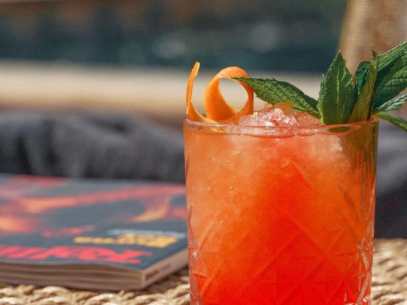 Bicchiere da cocktail rosso con ghiaccio e menta su tavolo intrecciato all'aperto.