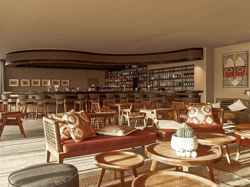 Lounge luminosa dell'hotel con comode sedute, mobili in legno e bar sullo sfondo.