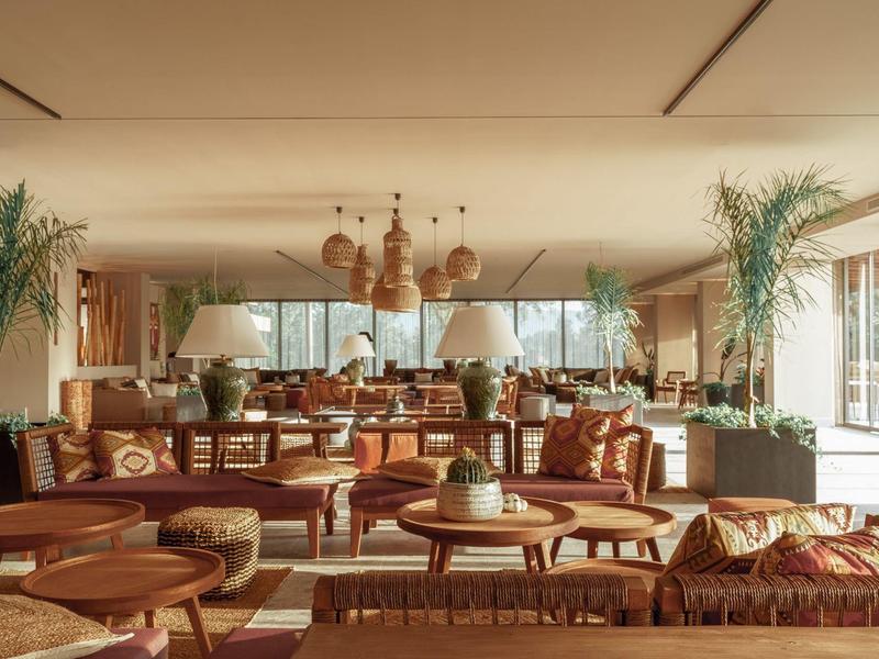 Un'area lounge d'hotel arredata con calore con mobili in legno e rattan e lampade sospese.