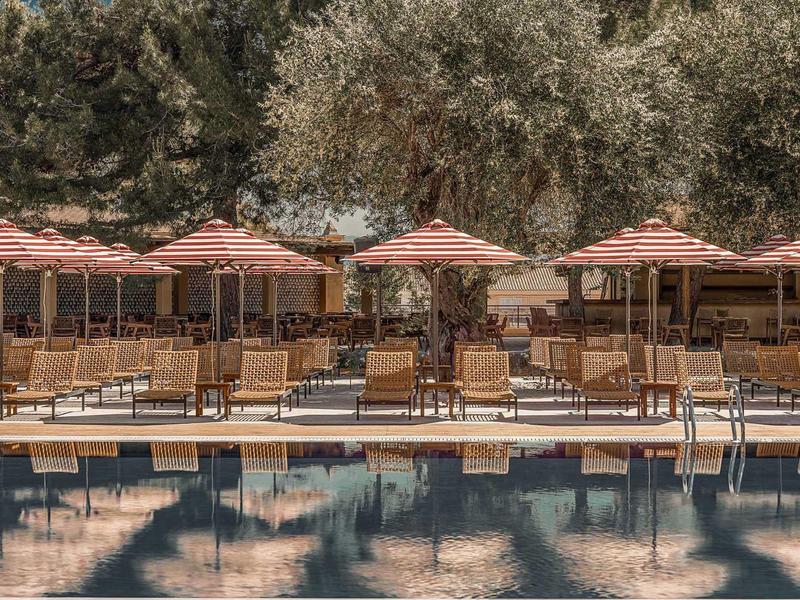 Area piscina vuota con ombrelloni e sedie sotto grandi alberi all'hotel.