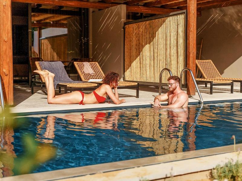 Due persone si rilassano a una piscina vicino a un hotel con sdraio.