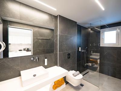 Modernes Badezimmer mit dunklen Wandfliesen, großer Spiegel, Waschtisch, Toilette und Dusche mit Glasabtrennung.