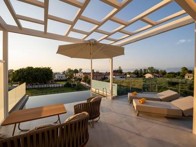 Terrasse mit Pool, Sonnenliege, Stühlen, großem Sonnenschirm und weitem Blick ins Grüne bei Sonnenuntergang.