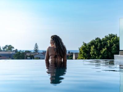 Frau im Pool mit schulterlangem Haar, klare Wasseroberfläche und blauer Himmel im Hintergrund.