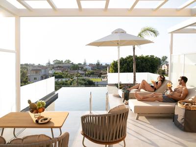 Moderne Terrasse mit Pool, Sonnenschirm, Liegen, Tisch, Stühlen und zwei entspannten Personen.