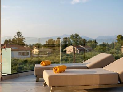 Terrassenliegen mit gelben Handtüchern, Glasgeländer, Häuser und Berge im Hintergrund.