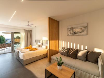 Helles Wohnzimmer mit Sofa, Holztisch, Bett und offenem Balkon mit grünen Pflanzen.