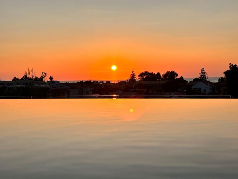 Tramonto con cielo arancione e acqua calma, probabilmente una piscina in primo piano.