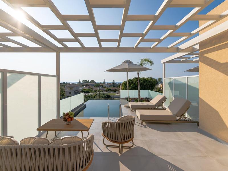 Terrazza sul tetto con area salotto, lettini, piscina e vista sulla città con sole.