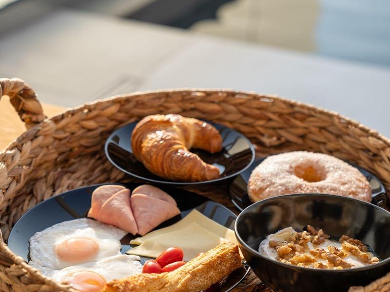 Cesto per la colazione con uovo fritto, croissant, ciambella, prosciutto, cereali e pancake vicino alla piscina.
