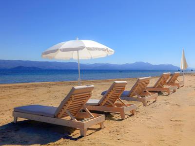 Leere Liegestühle mit Sonnenschirm am Strand, Meer und Berglandschaft im Hintergrund.