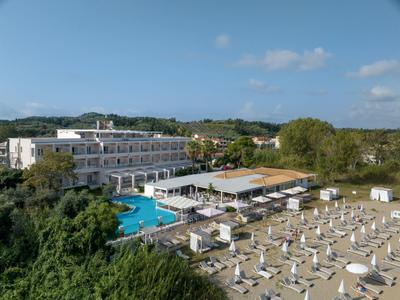 Hotel mit Pool, vielen Sonnenschirmen und Liegen in grüner Landschaft bei klarem Himmel.