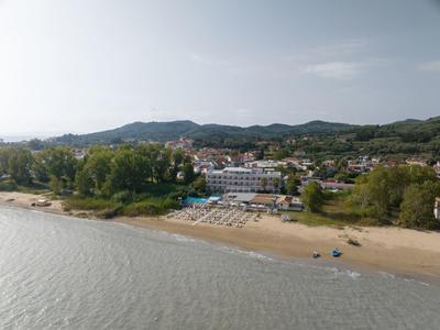 Hotelanlage am Sandstrand mit Liegestühlen und bewaldeten Hügeln im Hintergrund.