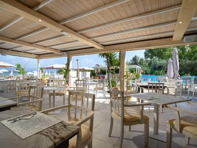 Offener Hotelrestaurantbereich mit Holztischen unter Holzdach am Pool und Blick auf das Meer.